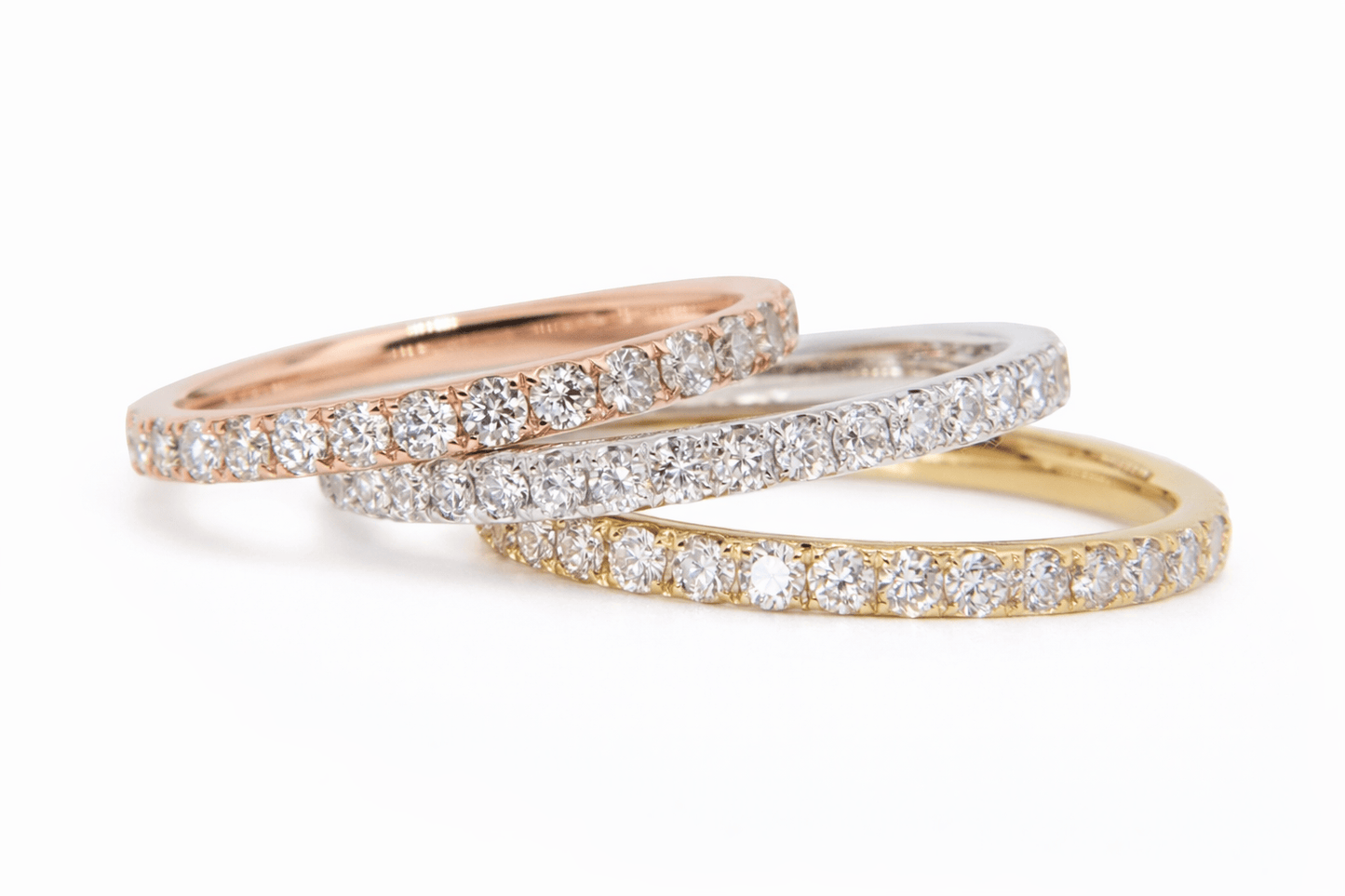 Three diamond-studded rings in rose gold, white gold, and yellow gold on a white background.