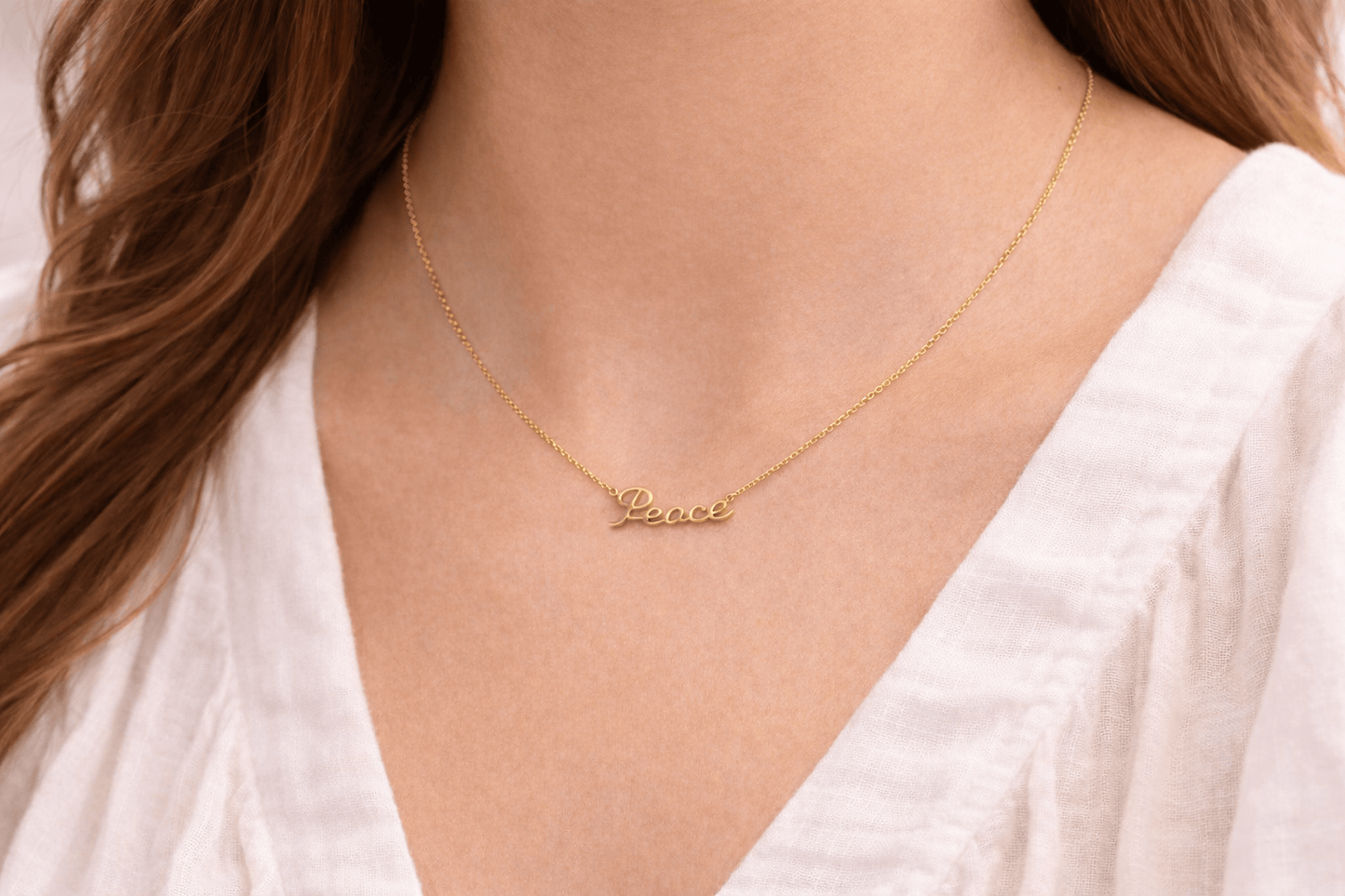 Gold necklace with 'Peace' pendant worn by a person in a white top